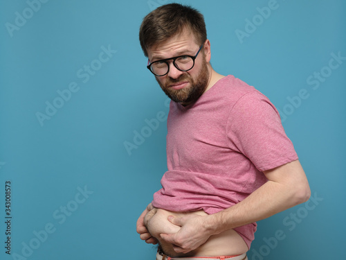 Upset man shows and holds with hands his excess fat on his stomach. Copy space. Overweight person. Healthy lifestyle concept. photo