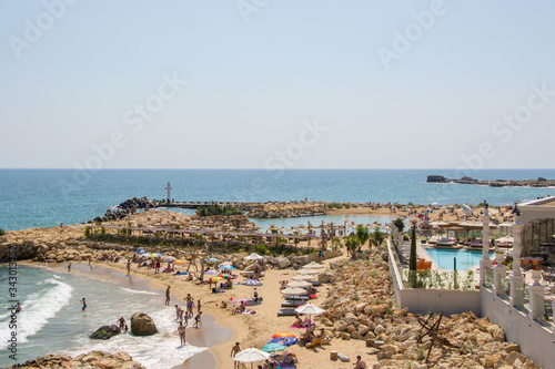 People on the beach, having fun next to luxury hotel on the coastline, pool, umbrellas and beach chairs