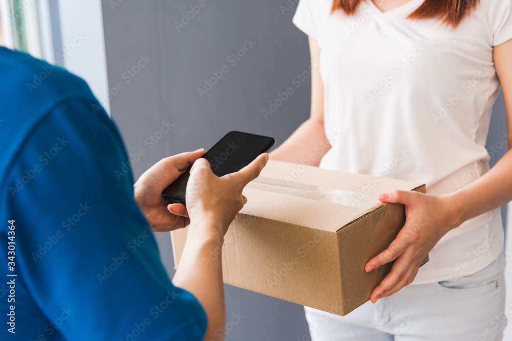 Asian young delivery man courier shopping online with package post box in uniform wearing protective face mask making service woman customer using hand finger signature on digital mobile phone at home Asian young delivery man courier shopping online with package post box in uniform wearing protective face mask making service woman customer using hand finger signature on digital mobile phone at home
