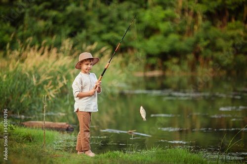 child boy engaged in fishing hobbies. he stands on the riverbank in the summer and holds a fishing rod with caught fish