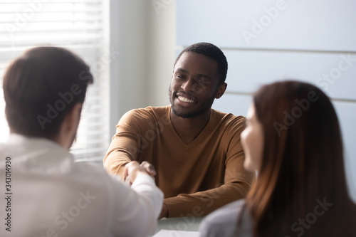 Smiling african american candidate shaking hands with businessman at job interview in office. Managers greeting client, good business partners negotiation.