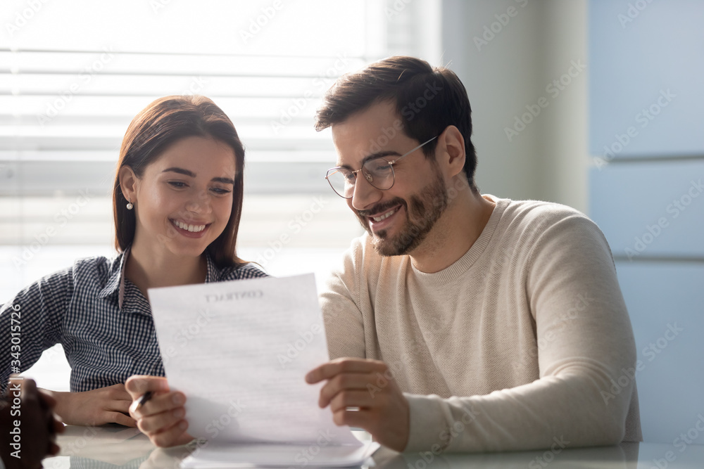 Young successful couple, man and woman reading business document at mortgage negotiating. Happy smiling husband in glasses and wife making deal together in broker office. Young successful couple, man and woman reading business document at mortgage negotiating. Happy smiling husband in glasses and wife making deal together in broker office.