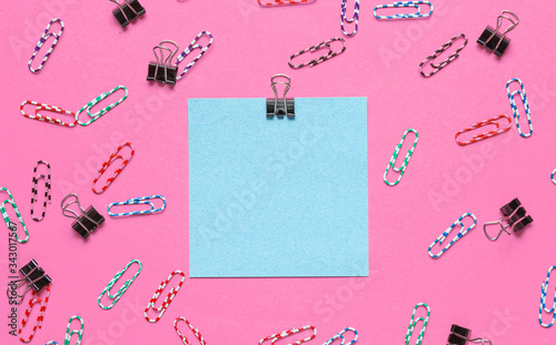 Stationery office supplies. Blue memo paper, paper clip on pink background. Top view