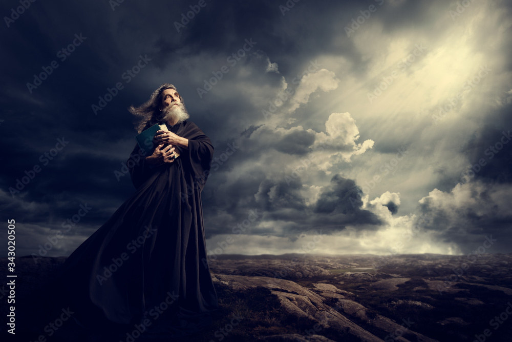 Monk Holding Bible Looking Up to God Sky Light, Old Priest in Black Robe in Storm Mountains Monk Holding Bible Looking Up to God Sky Light, Old Priest in Black Robe in Storm Mountains