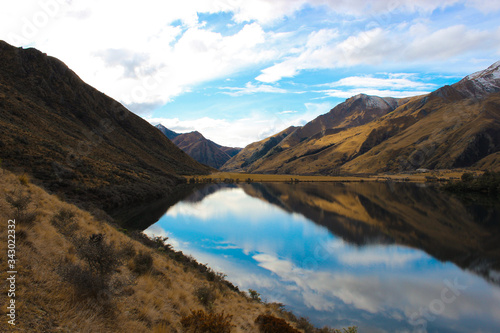 Reflections of Moke Lake, Otago, New Zealand. Still water, backed by snow capped mountains and grassy plains. 