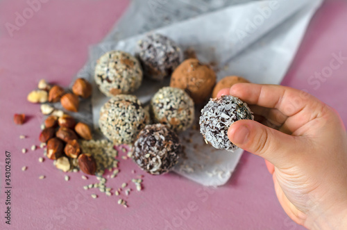 The child holds in his hand the Energy Bols - homemad raw candy. Mixed dates, nuts, dried fruits, sprinkled with coconut, cocoa and sesame seeds. The concept of healthy sweets. Paleo, keto diet. © Анастасия Савченко