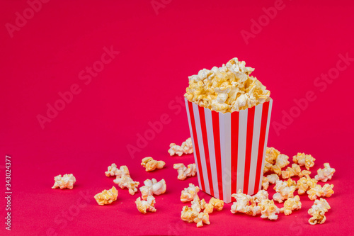 Paper cup with popcorn on color background. Striped box with popcorn on red background.Popcorn in red and white striped cardboard bucket .