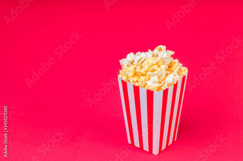Paper cup with popcorn on color background. Striped box with popcorn on red background.Popcorn in red and white striped cardboard bucket .