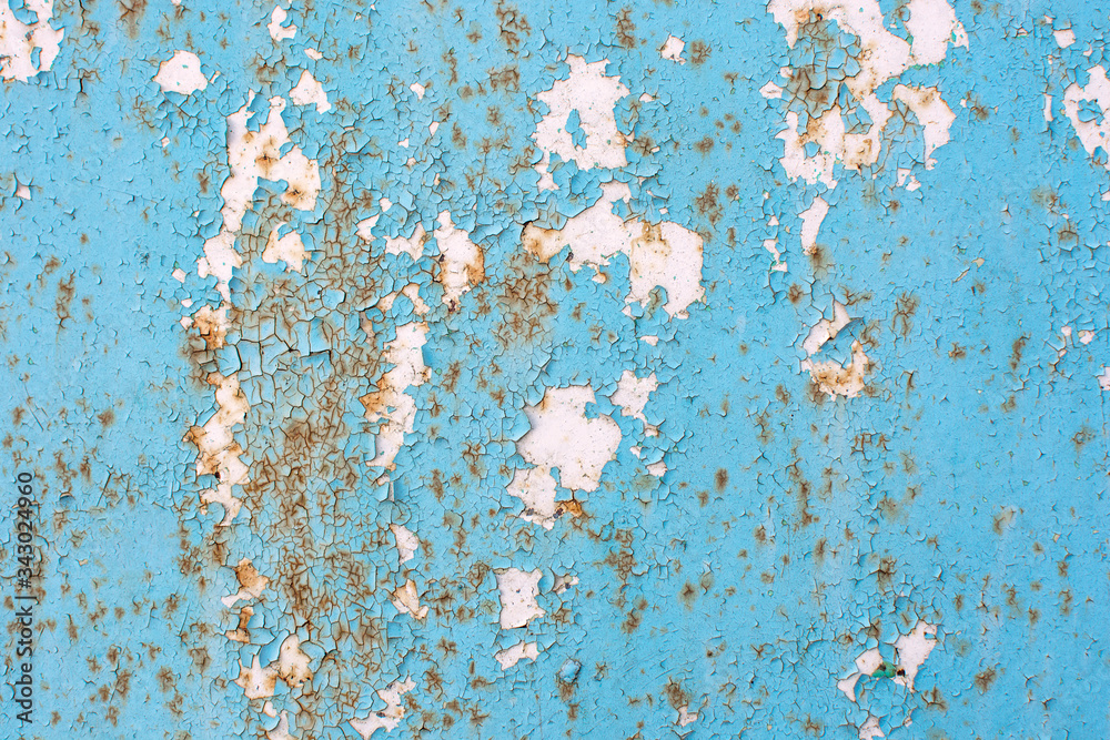 Old cracked blue paint covers the white metal wall. The paint was peeling, cracked, and peeling in places. White spots formed. There are traces of rust. Close-up photo, cropped.