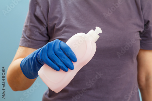 Woman holding a bottle of dishwashing liquid on a blue background.