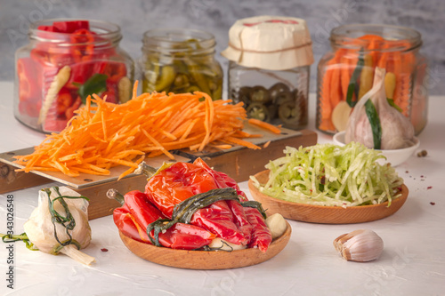 Fermented red hot peppers to enhance immunity with spices and grated carrots on a hand grater on a light wooden table against a background of glass jars with pickled products