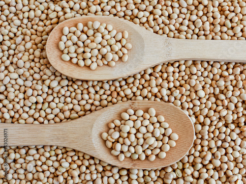 Soya in a wooden spoon, top view on a background of scattered soybeans. Vegan. Natural food. Suitable for background.