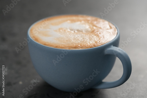 Fresh cappuccino in blue cup on concrete background