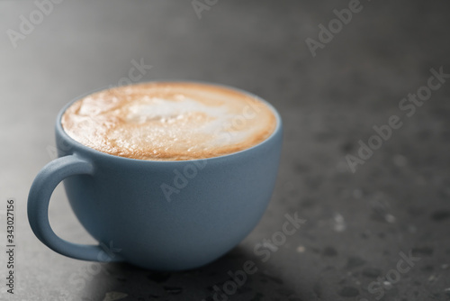 Fresh cappuccino in blue cup on concrete background