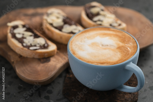 Fresh cappuccino in blue cup with toasts with chocolate spread on concrete background