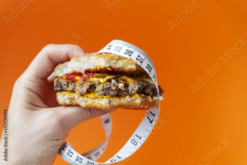Gamburgers with centimeter in the hand on the orange color. Diet concept. Copy space. Place for text and design.