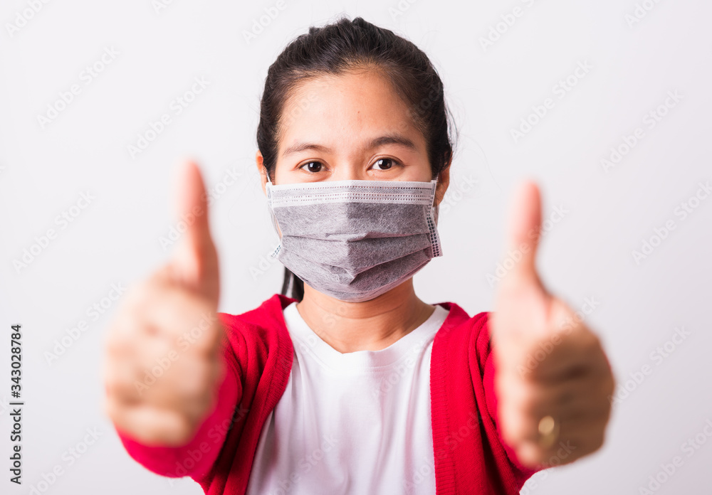 Asian adult woman wearing red shirt and face mask protective against coronavirus or COVID-19 virus or filter dust, air pollution her show finger thumb up for good sign, isolated white background Asian adult woman wearing red shirt and face mask protective against coronavirus or COVID-19 virus or filter dust, air pollution her show finger thumb up for good sign, isolated white background