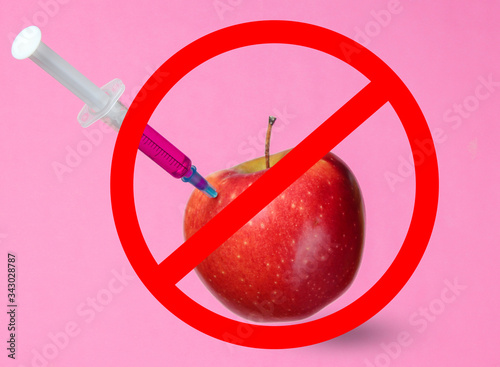Genetically modified Red Apple with syringes on pink background with prohibition sign. Medical Syringe injecting GMO in apple, fruit concept minimal