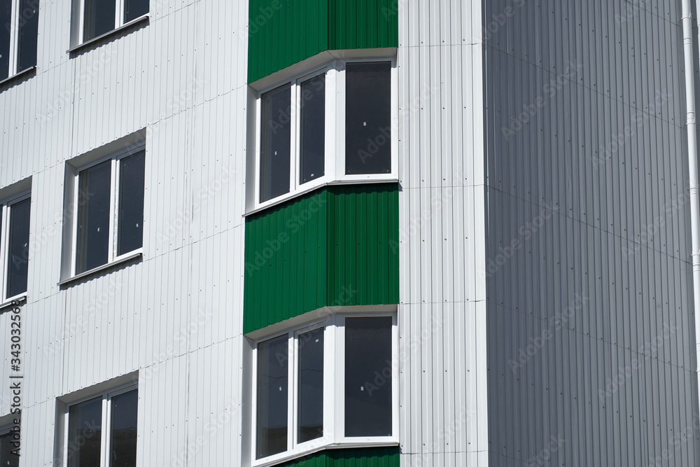 facade of a new multistory building with white and green metal siding, many Windows