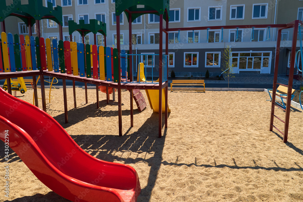 Urban residential infrastructure without people - children's playground next to a condominium. Swing, slide, stairs, multistory building. A place for children to play. Urban residential infrastructure without people - children's playground next to a condominium. Swing, slide, stairs, multistory building. A place for children to play.