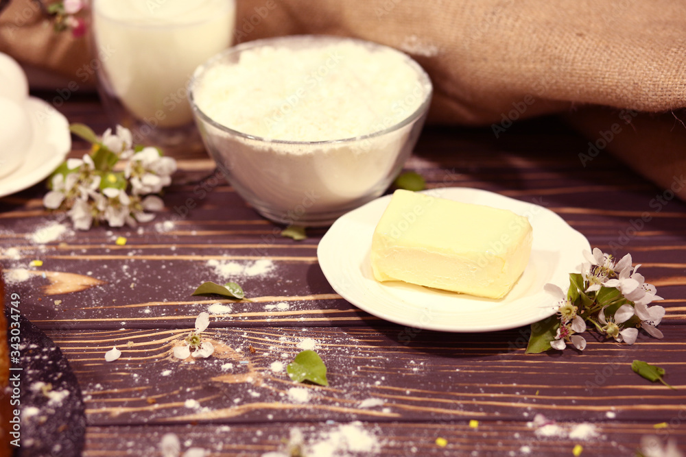 butter, a bowl with flour, a glass of milk, eggs, homemade cakes and flowers on an old wooden background. Ingredients for cooking. Black and white. The near plan. Healthy eating concept butter, a bowl with flour, a glass of milk, eggs, homemade cakes and flowers on an old wooden background. Ingredients for cooking. Black and white. The near plan. Healthy eating concept