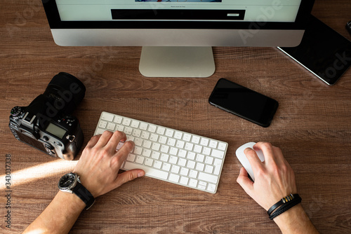 Man works at a computer, hands on a keyboard, a camera, a phone. Home work concept. Top view.