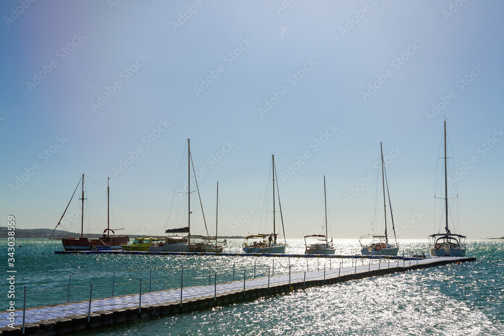 Several yachts in a row are parked at the pier. Blue sky and sea in the background. Skyline