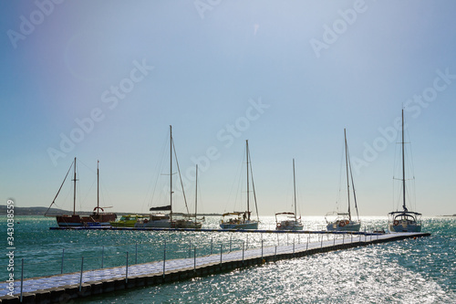 Several yachts in a row are parked at the pier. Blue sky and sea in the background. Skyline