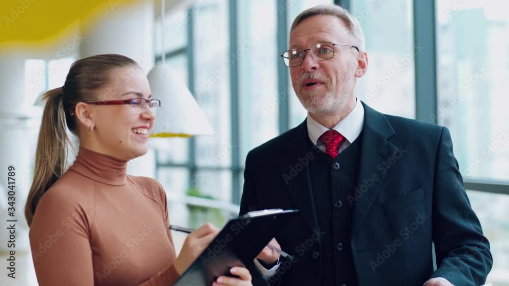 Smiling old businessman and a female secretary. Young woman talking with a mature man in costume in the modern office. Smiling old businessman and a female secretary. Young woman talking with a mature man in costume in the modern office.
