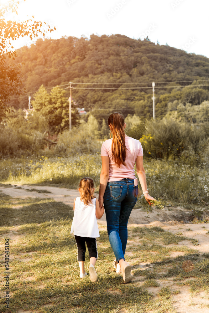 Fototapeta premium Beautiful couple child girl with mother are walking in spring garden with pink blossom roses flowers, sunset time