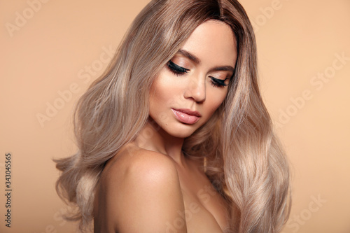 Ombre blond wavy hairstyle. Beauty fashion blonde woman portrait. Beautiful girl model with makeup  long healthy hair style posing isolated on studio beige background.
