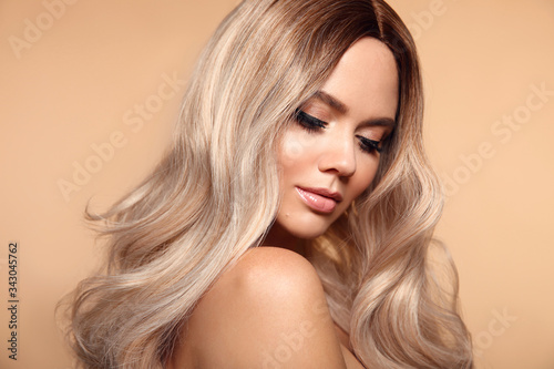 Ombre blond wavy hairstyle. Beauty fashion blonde woman portrait. Beautiful girl model with makeup, long healthy hair style posing isolated on studio beige background. photo