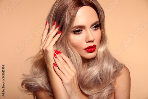 Makeup, manicured nails. Beauty portrait of blonde woman with red lips, long healthy shiny blond hair style. Sensual girl with bright makeup isolated on beige backhround.