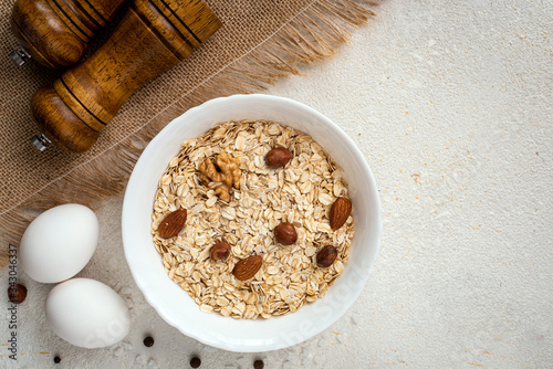 Dry oatmeal with nuts and eggs in a white plate on a white background. Healthy breakfast concept. Top view, copy space.
