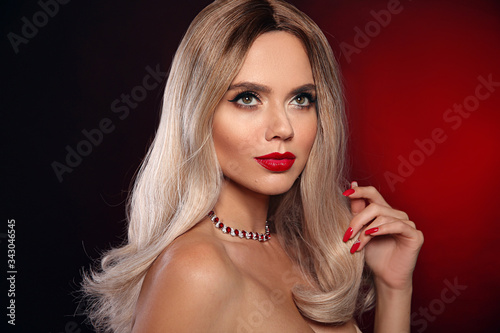 Ruby pendant jewelry. Beauty portrait of blonde woman with red lips, long healthy shiny blond hair style and manicured nails. Sensual girl with bright makeup isolated on dark studio backhround.
