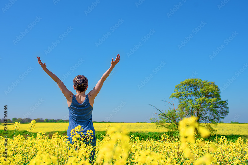 Happy woman wearing blue top and jeans raised her hands high against blu sky and yellow rapeseed fields Happy woman wearing blue top and jeans raised her hands high against blu sky and yellow rapeseed fields