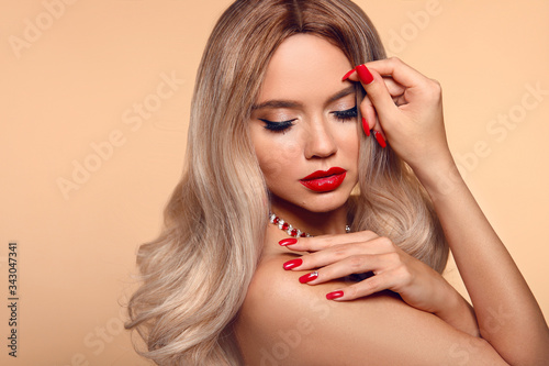 Makeup   manicured nails. Beauty portrait of blonde woman with red lips  long healthy shiny blond hair style. Sensual girl with bright makeup isolated on beige backhround.