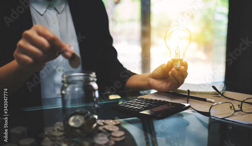 Businesswoman holding a light bulb while putting coin into a glass jar for saving energy and money concept