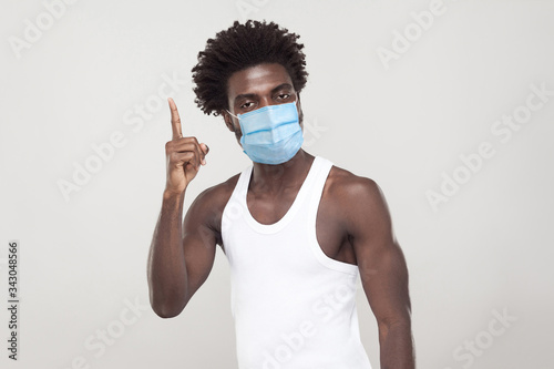 I have Idea. Portrait of young man wearing white shirt with surgical medical mask standing holding finger up and looking at camera. indoor studio shot isolated on gray background.