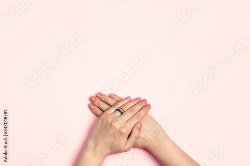 Female hands with a wedding ring from a rainbow ribbon on a pink background. Lesbian marriage proposal.