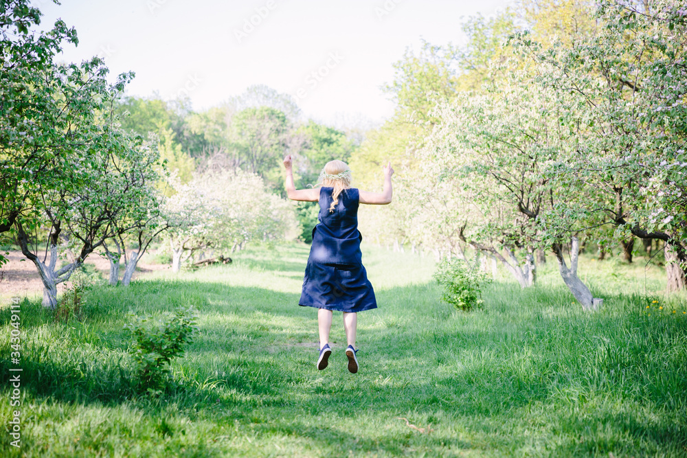 Back view of a woman walks in the sunny summer season park. The beautiful lady walking near trees Back view of lonely blonde woman standing on the sunny path in the park.