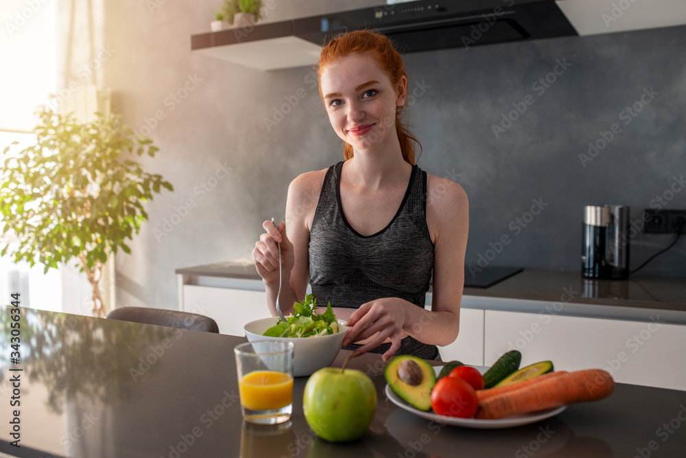 Athletic girl with gym clothes eats a salad in the kitchen Athletic girl with gym clothes eats a salad in the kitchen