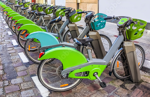 Electric rental bikes, green and gray, locked on their chargers.