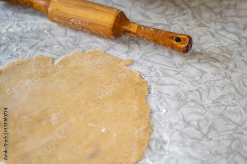 The rolling pin lies on the kitchen table next to the rolled dough ready for cooking.