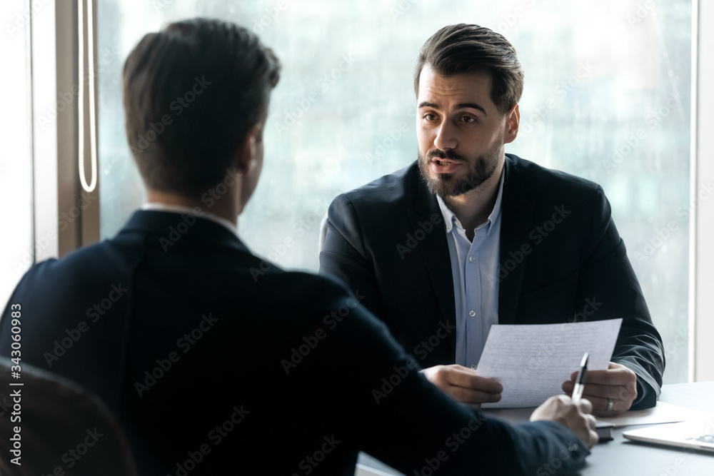 Confident hr manager asking questions to candidate on job interview, sitting at desk, holding cv in hands, business partners discussing project strategy, team leader giving instructions to intern Confident hr manager asking questions to candidate on job interview, sitting at desk, holding cv in hands, business partners discussing project strategy, team leader giving instructions to intern