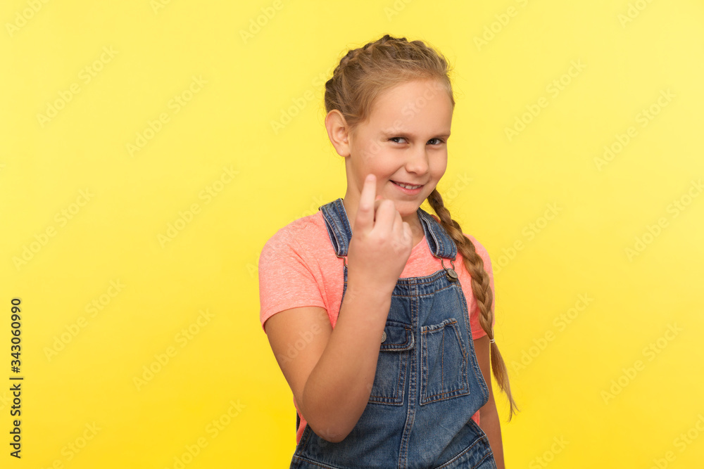 Approach to me! Portrait of cheerful cunning little girl with braid in denim overalls gesturing come here and smiling slyly, inviting with beckoning finger. studio shot isolated on yellow background Approach to me! Portrait of cheerful cunning little girl with braid in denim overalls gesturing come here and smiling slyly, inviting with beckoning finger. studio shot isolated on yellow background