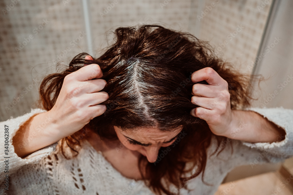 Naklejka premium .Young woman coloring her white hair in her bathroom. Hairdressers closed due to quarantine caused by covid19. Lifestyle