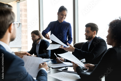 Smiling businesswoman coach giving handout material, paper sheets to employees at briefing, leader boss presenting financial report, project plan, business strategy documents at corporate meeting photo