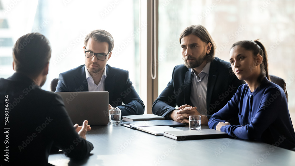 Three interested attentive hr managers listening to candidate on interview, sitting at table in boardroom, applicant seeker answering recruiters questions, colleagues looking at mentor coach