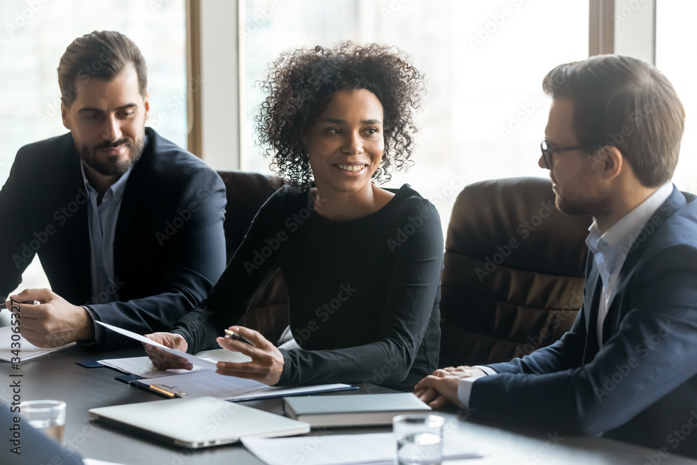 Smiling African American businesswoman speaking at corporate meeting in boardroom, sitting at table, business partners discussing contract terms, colleagues sharing ideas at briefing - obrazy, fototapety, plakaty 